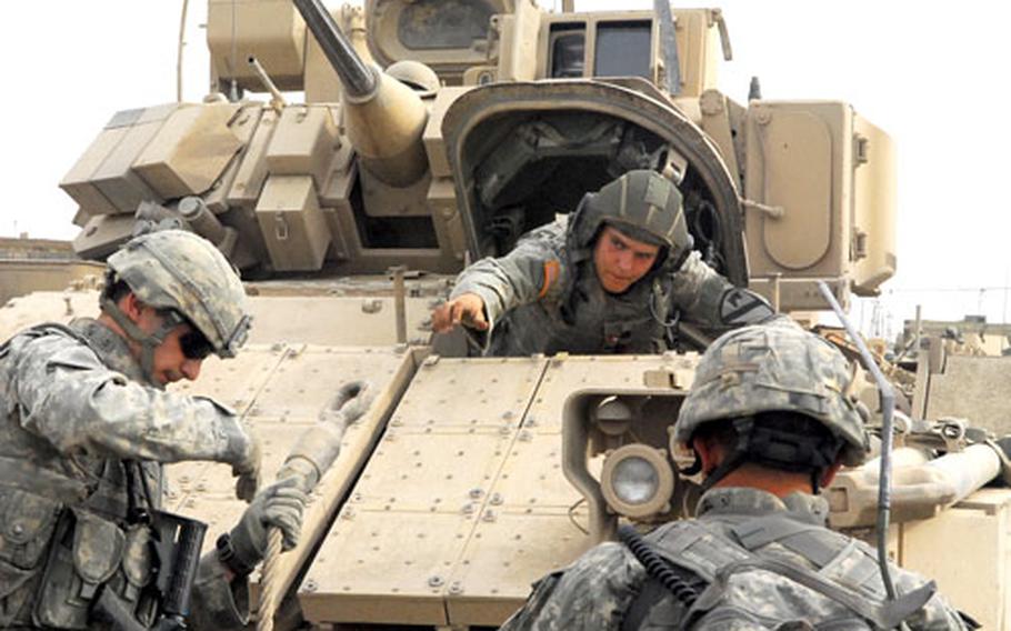 Spc. Krzysztof Socha, left, Pfc. Brit Wooten, inside the Bradley Fighting Vehicle, and Sgt. 1st Class John Wheatley prepare to pull a Humvee out of a mud field Monday.