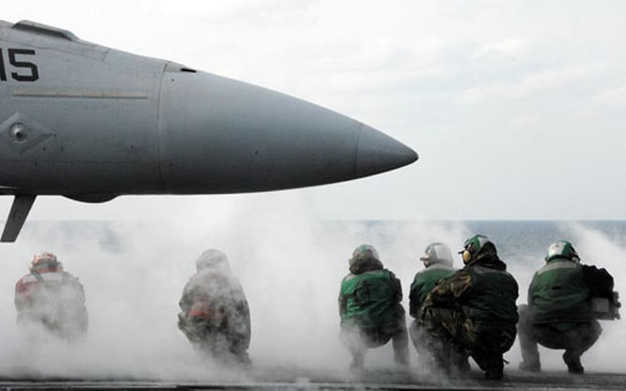 Sailors crouch on the flight deck of the U.S.S. Nimitz as a jet takes off.