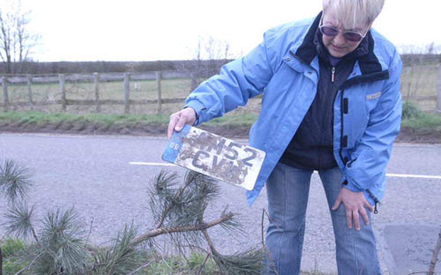 Ros Norman, who owns Dachel Stud on Barton Mills Road near Mildenhall, picks up a license plate that flew off during recent car accident. Three drivers in the past three months have swerved off the road in the same place. Barton Mills is a busy thoroughfare between the A-11 and the A-14 and poses a dangerous curve near Norman&#39;s property.