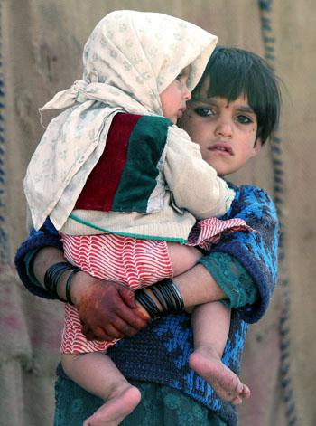 A girl holds a baby as she watches U.S. soldiers meet with an elder in the village of Mama Karez.