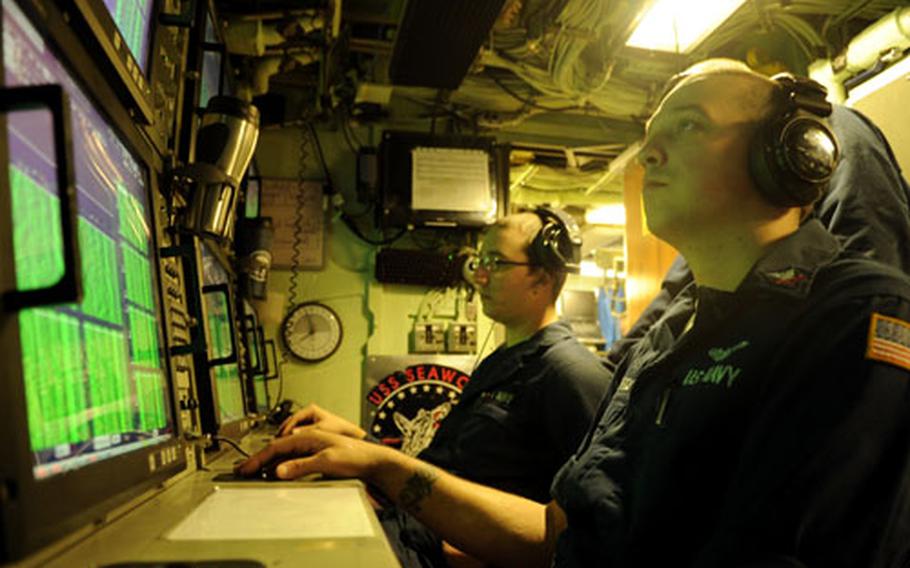 Petty Officer 2nd Class Jeremy Edwards, foreground, and Seaman Anthony Terry listen by isolating the green bands on their displays in the sonar room.
