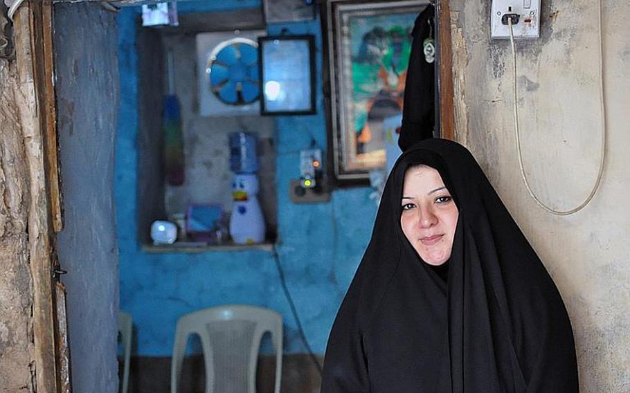 Aklas Farhood, who was widowed when her husband was killed in a Baghdad bombing, stands in front of the tiny room that she lives in with her two sons.