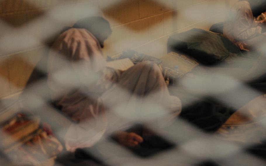 A detainee at the U.S. Detention Facility in Parwan reads a book in his cell, a large, caged room housing about 20 men. Prison rules forbid the photographing of detainee faces.
