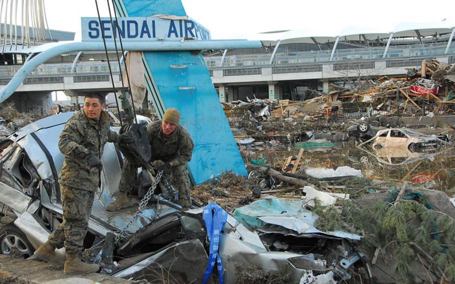 Staff Sgt. Hugo Roman, left, and Lance Cpl. Kyle White, both of the Combined Arms Training Center at Camp Fuji, remove the remnants of a vehicle from Sendai Airport.