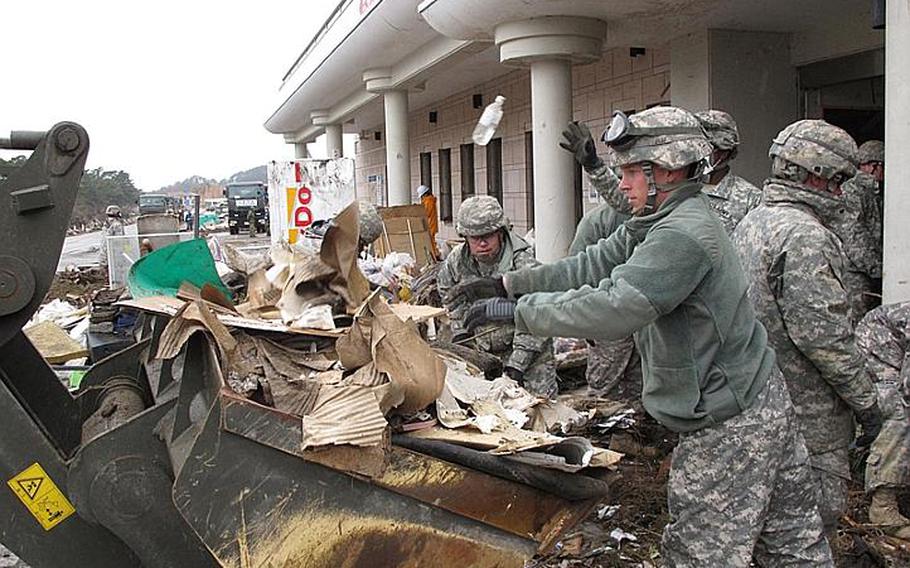 Spc. Timothy Jones, right, and Spc. Ivan Santos, background center, toss debris while clearing out Nobiru train station, in Japan's tsunami-battered northeast, in April 2011.
