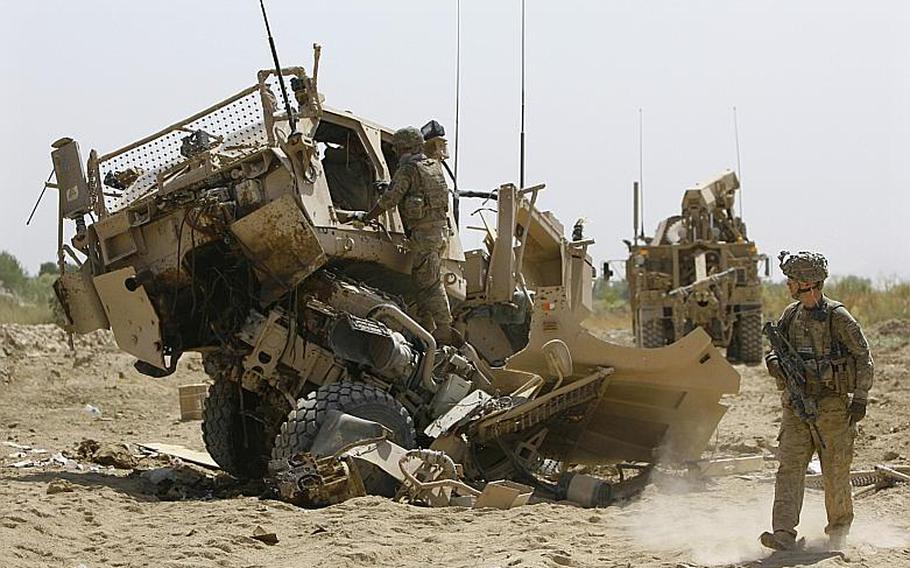 Company C Commander Capt. Dennis Call walks past a destroyed M-ATV while a member of the Explosive Ordnance Disposal team looks in the cab following an improved explosive device attack that killed five soldiers near Combat Outpost Nalgham in Afghanistan on August 11, 2011.
