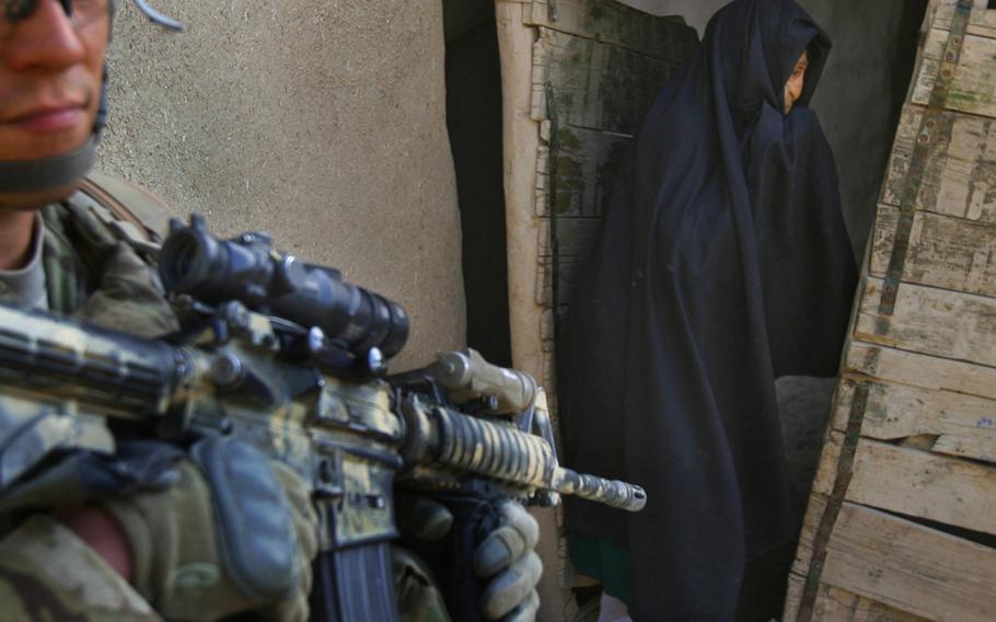 An Afghan woman emerges from her home as Sgt. Robert Hogeland of Company F, 4th Battalion, 101st Aviation Regiment, 159th Combat Aviation Brigade, 101st Airborne Division, patrols the village of Loy Shur with Afghan National Army soldiers on Sept. 23, 2011, in Zabul province, Afghanistan.