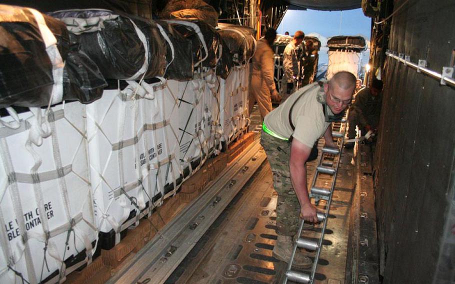 Senior Airman Phillip Underwood replaces a broken roller in the cargo bay of a C-130 while the plane waits before dawn to take off on an airdrop resupply mission. Gravity will pull the white cargo bundles fitted with parachutes out of the back of the plane when the pilot goes into a climb above a remote drop zone where soldiers will be waiting.