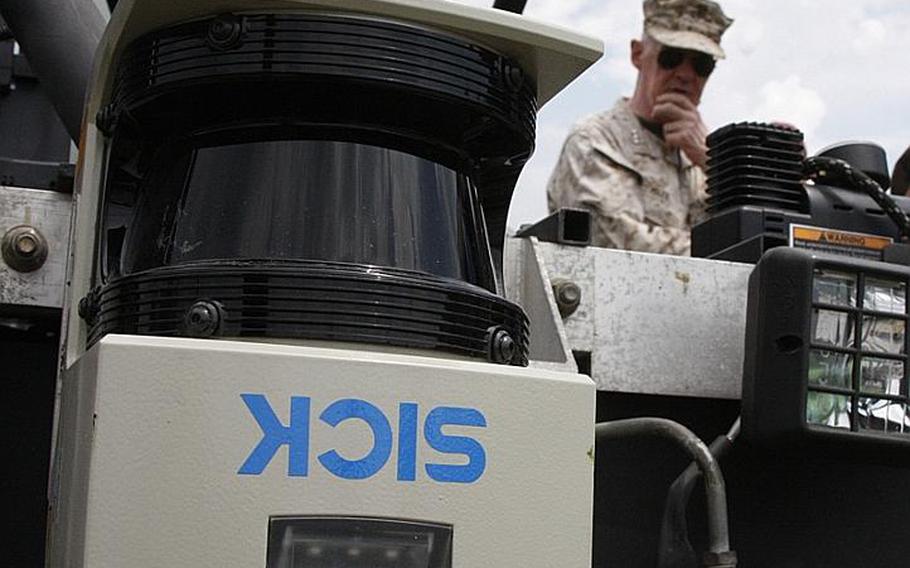 A rotating laser sensor on the front of an autonomous HEAT electric vehicle helps the system build a computer map of the world around it, a necessity for navigating in the field. In the background, Marine Lt. Gen. Richard Mills, commander of Marine Corps Combat Development Command, examines the vehicle at Fort Pickett, Va., on July 30, 2012.