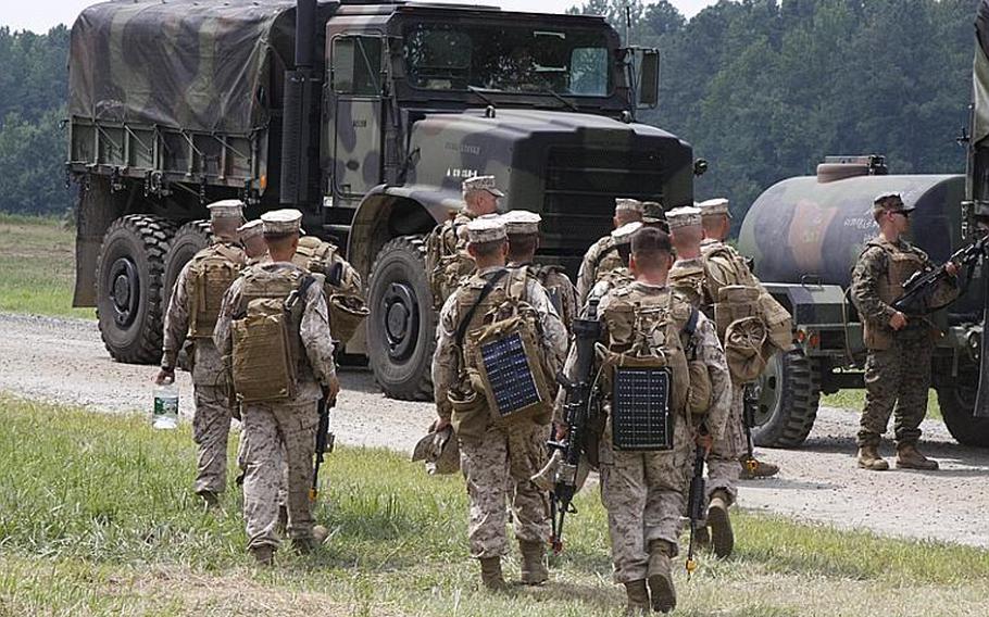 A squad of Marines, some carrying advanced solar charging equipment on their packs, files toward a supply convoy partially made up of robotic vehicles at Fort Pickett, Va., on July 30, 2012.