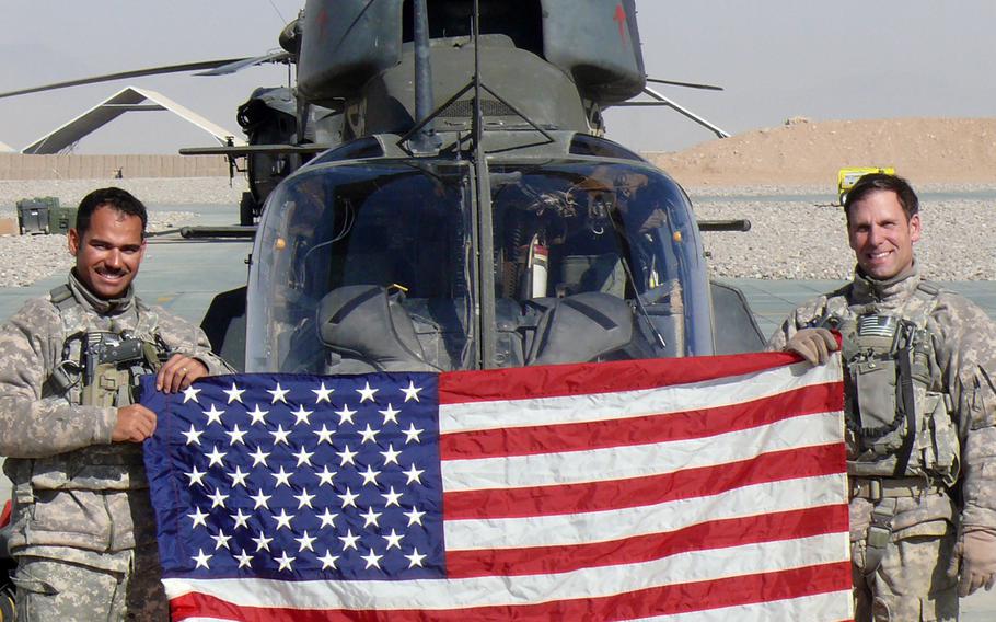 Army Chief Warrant Officer 3 Omar Torres (left) and Chief Warrant Officer 3 Matthew McEvers (right) hold the flag in front of their Kiowa OH-58D at Forward Operating Base Tarin Kowt in Uruzgan Province. The men were both awarded the Distinguished Flying Cross for a Nov. 11, 2009 mission during that tour.