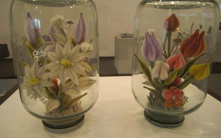 Bouquets are made of pipe cleaners and glass mayonnaise jars. Adding color to daily life with decoration like this played a critical role for mental survival for the people confined in POW camps in World War II.