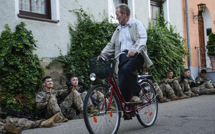 A bicycle rider pedals past U.S. soldiers with 2nd Platoon,  3rd Squadron, 2nd Cavalry Regiment in a Bavarian village on Aug. 2, 2013. The soldiers were taking a break in  their 18.36-mile ruck march from Sulzbach-Rosenberg, Germany, back to Rose Barracks in Vilseck.