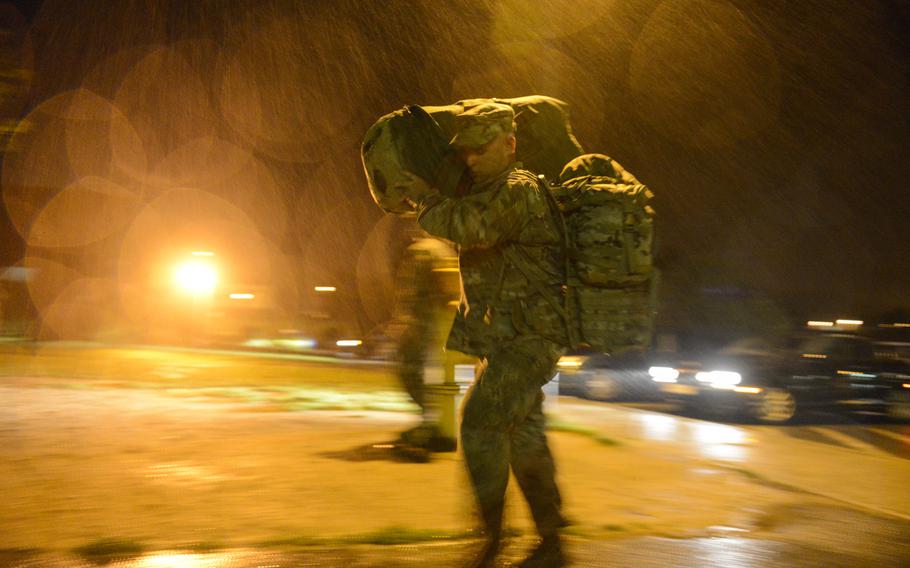 Staff Sgt. Floyd Combs carries his duffle bag and rucksack in the rain at the beginning of a long day of processing for a nine-month deployment to Afghanistan, Aug. 26, 2013.