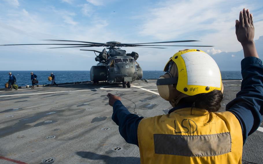 Petty Officer 2nd Class Cost Dumervil, a boatswain's mate, directs the flight deck crew as an MH-53E Sea Dragon helicopter lands on the flight deck of the amphibious dock landing ship USS Gunston Hall on Dec. 7, 2013.