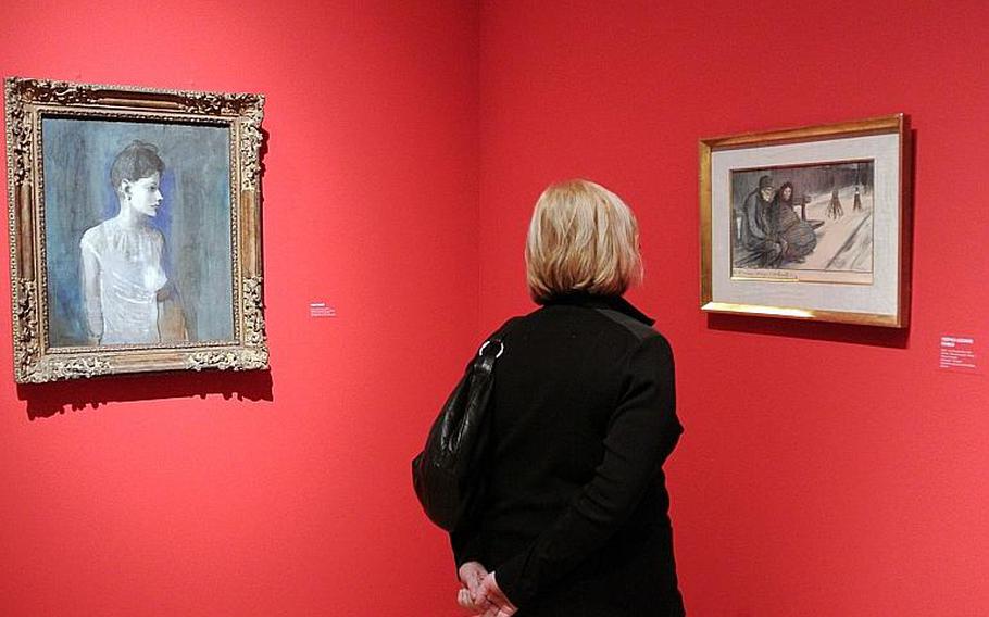 A visitor to the "Esprit Montmartre: Bohemian Life in Paris around 1900" exhibit at the Schirn Kunsthalle in Frankfurt, Germany, takes a closer look at Théophile Steinlen's "Hiver - Les Pouvres Gens" from 1901, Thursday, Feb. 6, 2014. At left is Pablo Picasso's "Femme a la chemise," from about 1905.