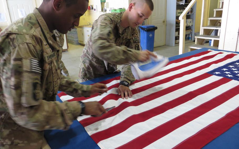 Pfc. Durell Siverand, left, and Pfc. Alex Valdivia, mortuary affairs specialists with the 54th Quartermaster Company, prepare a flag that will cover a transfer case carrying the remains of a U.S. servicemember from Bagram Air Field in Afghanistan to Dover Air Force Base in Delaware.