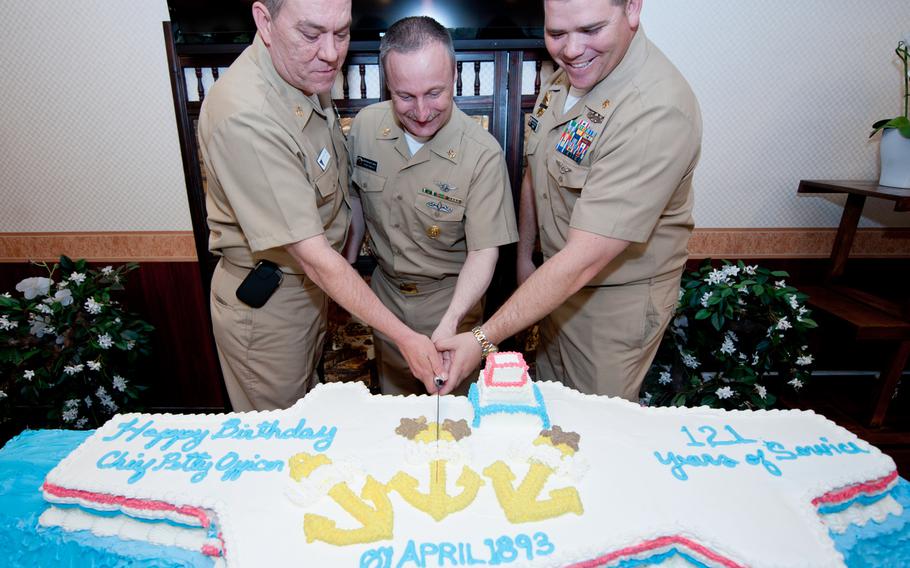 Naval Air Facility Atsugi Command Master Chief Michael Wilkins, center, cuts a cake with Command Master Chief Jason Eckard, of Carrier Air Wing 5, left, and Chief Petty Officer Julius Olguin, of Naval Security Force Atsugi, Japan. They represent the oldest and youngest members of the Chief Petty Officers' Mess present, during a chief petty officers' birthday celebration at Naval Air Facility Atsugi, Japan, on April 1, 2014.