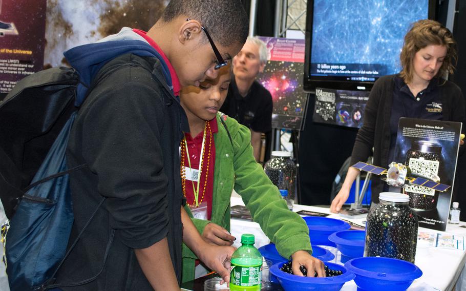 Two young kids learn how much dark matter is in the universe at a NASA exhibit at the USA Science and Engineering Festival on April 25, 2014 in Washington, D.C. The black marbles represent dark matter while the colored marbles - the very few of them - represent what we know of the universe. 