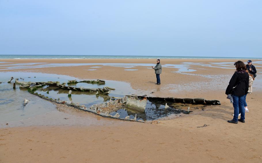 Visitors look at the remains of a world War II landing craft sunk in the sands of Omaha Beach below the Normandy American Cemetery in April 2014.