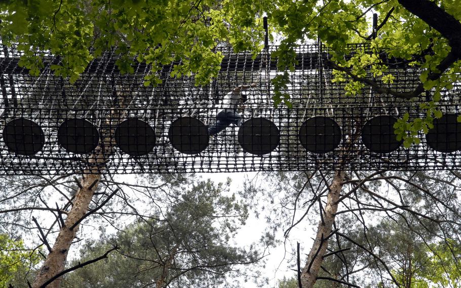 A person traverses the metal discs that make up a segment of the treetop trail near the town of Fischbach bei Dahn, Germany. The discs are suspended by chains and sway when stepped upon.