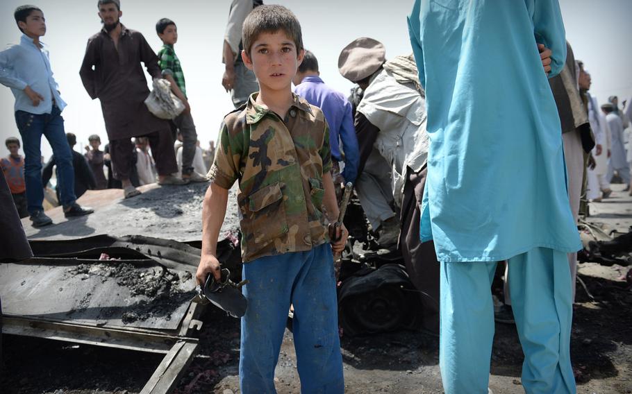 An Afghan boy joins the crowd salvaging scraps from the remains of a truck bomb used by the Taliban to launch an attack near the Kabul airport on Thursday, July 17, 2014. After initially trying to preserve the scene, Afghan security officers gave up after being confronted by the crowd.