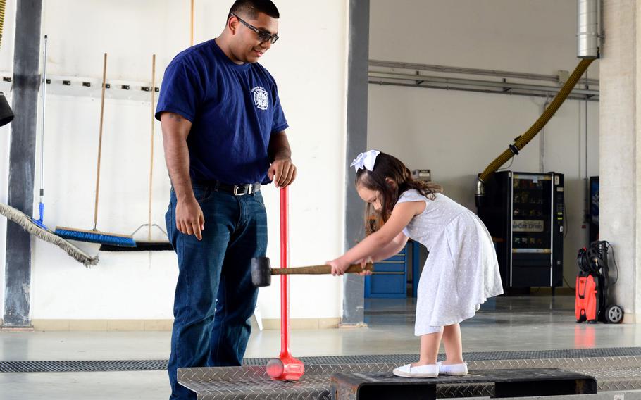 Senior Airman Manuel Rodriguez, 31st Civil Engineer Squadron firefighter, shows a child the proper way to strike a support beam during a fire department combat challenge on Oct. 5, 2014, at Aviano Air Base, Italy.