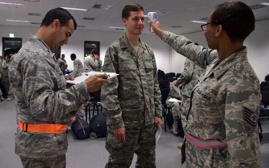 Airman 1st Class Mark Underhill has his temperature taken by Tech. Sgt. Saquadrea Crosby, right, as Lt. Col. Juan Ramirez logs the information at a passenger holding facility at Ramstein Air Base, Germany, Oct. 19, 2014.