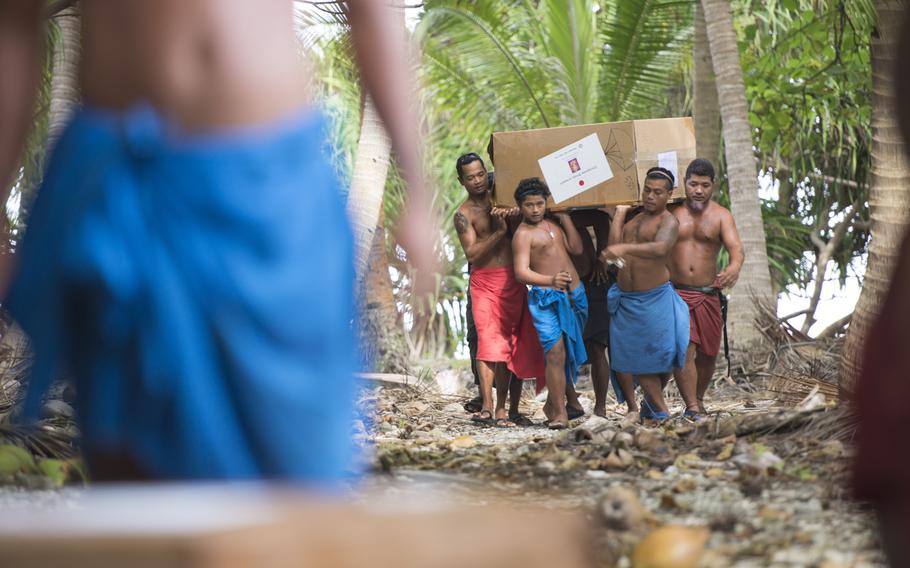 Islanders carry half of a bundle that dropped on their island during Operation Christmas Drop at Mogmog, Ulithi Atoll, on Dec. 9, 2014. Ongoing for 63 years, the drop delivers supplies including, food, clothing, medicine, tools and toys to the islanders.