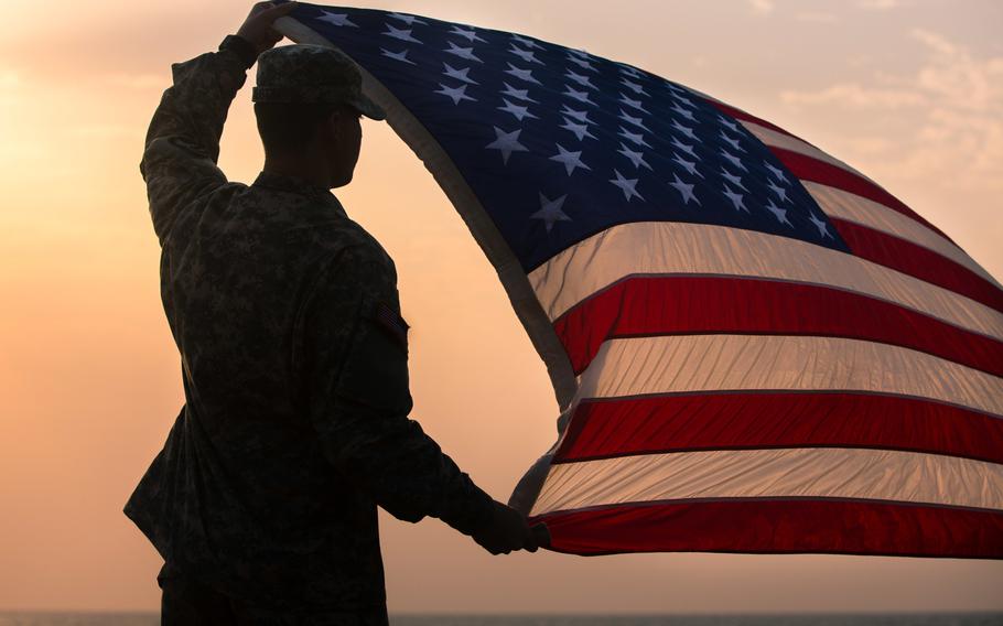 Spc. Morgan Austin, communications specialist with Joint Forces Command ? United Assistance, assigned to Headquarters and Headquarters Battalion, 101st Airborne Division (Air Assault), holds up the U.S. flag during a promotion and re-enlistment ceremony Jan. 1, 2015, at Barclay Training Center, Monrovia, Liberia.
