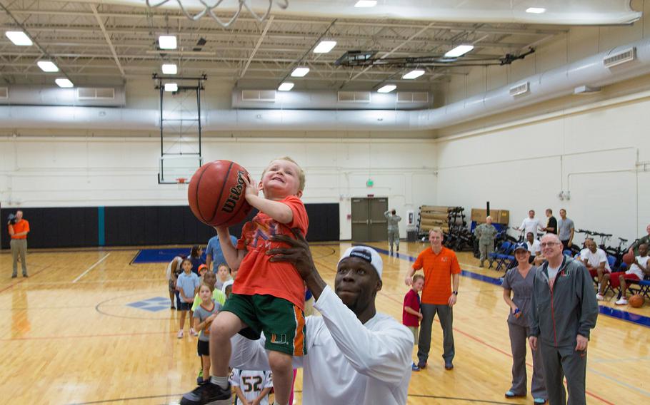 University of Miami men's basketball player Tonye Jekiri prepares to assist one of the children in dunking the basketball during the ''Night out with the Hurricanes'' event for military members and their families at the Sam Johnson Fitness Center, Homestead Air Reserve Base, Fla., on Jan. 6, 2015.