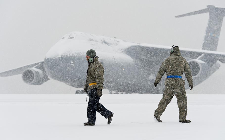 A snow-covered C-5M Super Galaxy sits in the background as two Team Dover members pass each other on the flight line Jan. 6, 2015, at Dover Air Force Base, Del.