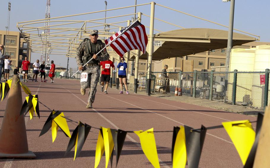 Sgt. Christopher Hughes, of the 43rd Sustainment Brigade, 4th Infantry Division, carries the American flag across the finish line at the Army Marathon Shadow Run on March 1, 2015, at Camp Arifjan, Kuwait.