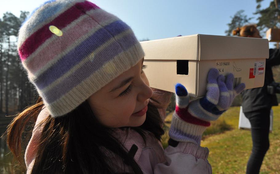 Ava Perez, 7, a second-grader at Ramstein Elementary School in Germany, peers through the small hole of a cardboard pinhole projector at the image of the partial solar eclipse Friday morning, March 20, 2015, on Ramstein Air Base.