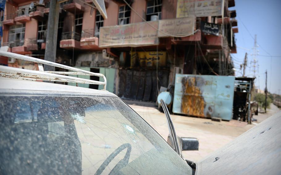 A bullet-damaged car sits in front of buildings burned and looted in downtown Tikrit, Iraq. The city sustained nearly a year of occupation by the Islamic State, then faced looting and other abuse by some liberators with the Iraqi security forces.