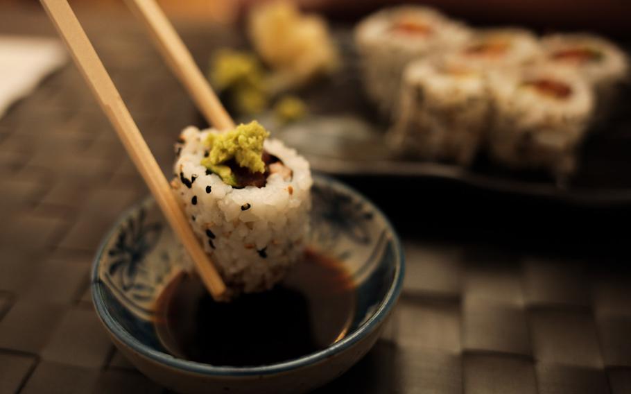A diner dips a piece of uramaki sushi with spicy tuna, avocado, cucumber and sesame into a tiny bowl of soy sauce at Ayami in Kaiserslautern, Germany.