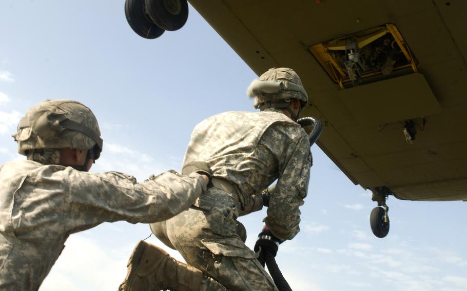 Two New York Army National Guard Soldiers from the 427th Brigade Support Battalion prepare to attach a sling load hook to a CH-47 Chinook helicopter, July 19, 2015, at Fort Drum, N.Y.