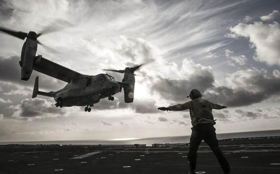 A U.S. Marine Corps MV-22 Osprey approaches the flight deck for a landing while being guided by a member of the flight crew. Marines with Marine Medium Tilt Rotor Squadron 166 Reinforced, the air-combat element of the 13th Marine Expeditionary Unit, work to land and stow aircraft in preparation for the Composite Training Unit Exercise, Oct. 19, 2015.