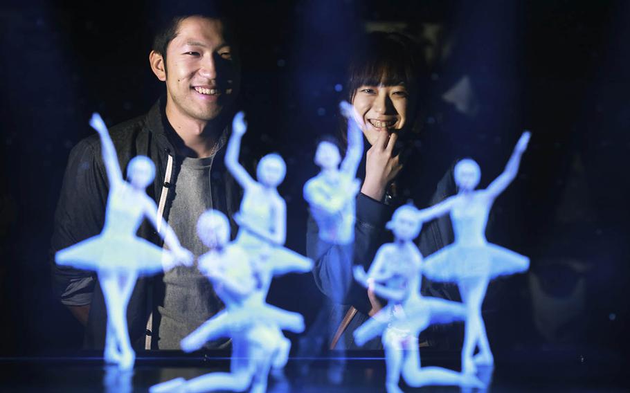 Tomoaki Ishizuka, left, and Yurika Yonekura, right, watch the hologram of Japanese skater Yuzuru Hanyu, center, with ballet dancers with their scanned faces attached April 28 at newly opened Hologram Dance Theater at Madame Tussauds in Tokyo. Madam Tussauds in Tokyo is launching an event allowing visitors to virtually join a 3-D world to dance with holograms of celebrities such as Brad Pitt, Leonardo DiCaprio and Lady Gaga.