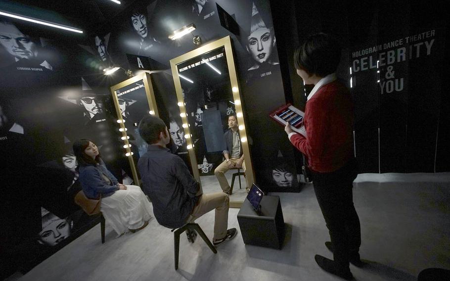 Tomoaki Ishizuka, center, and Yurika Yonekura, left, scan their faces April 28 as a staff member, right, guides them through a newly opened Hologram Dance Theater at Madame Tussauds in Tokyo.