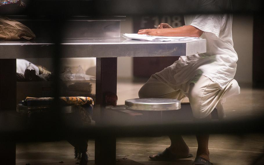 A detainee inside Camp VI at Guantanamo Bay, Cuba sits at a table inside the detention facility with pen and paper. Guantanamo Bay officials do not allow detainees' faces to be photographed at the facility because of operational security concerns.