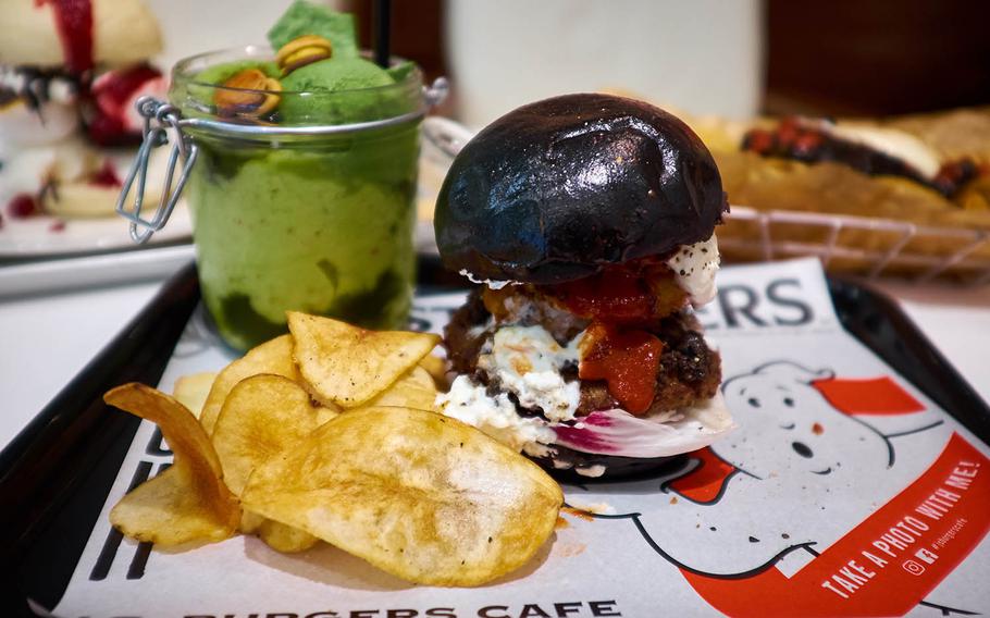The black bunned G.B. Burger headlines the new "Ghostbusters"-inspired menu at the upscale Tokyo-based burger chain J.S. Burgers Cafe. In the background is the Slimer-inspired Green Ghost Shake, an avocado and apple smoothie topped with matcha ice cream, a whole kiwi, two cherries and a pair of unexplainable burger-shaped cookies with chocolate cream filling.