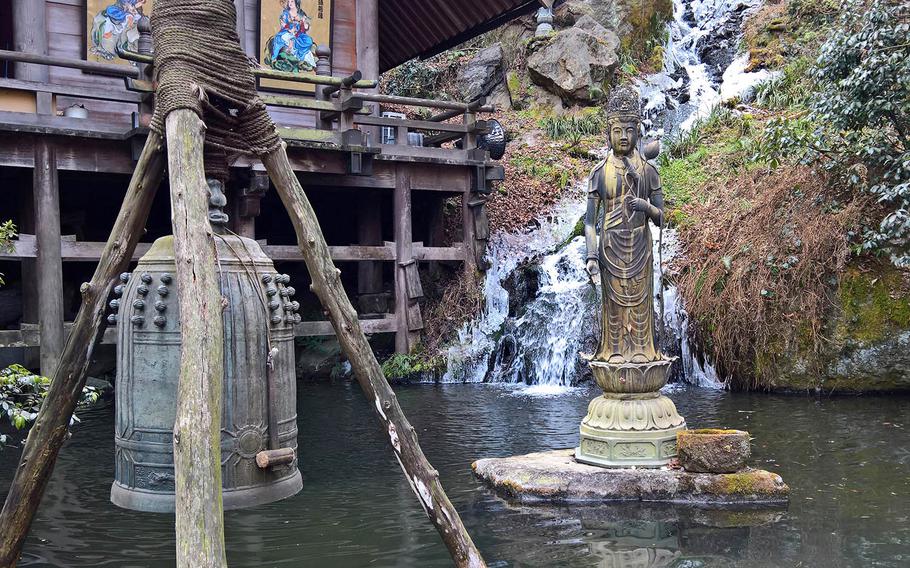 An outdoor dining area at Irori Sanzoku near Marine Corps Air Station Iwakuni, Japan, overlooks a serene waterfall and pond featuring a statue of Kannon Bodhisattva.