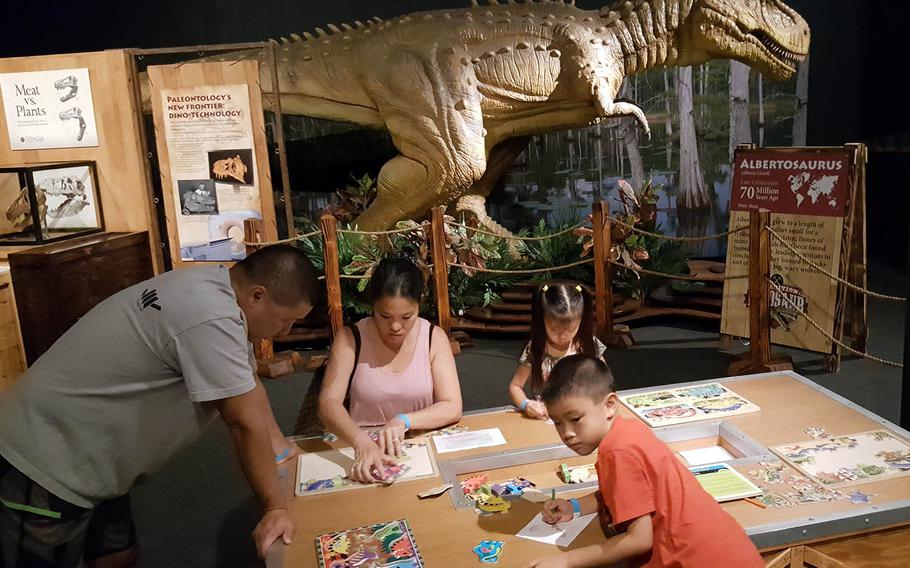 A family assembles puzzles as an Albertosaurus stands nearby at Expedition: Dinosaur at the Bishop Museum in Honolulu.