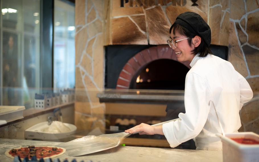 Maruolina, a chef at Pinoccio in Sasebo, gets ready to place a customer's pizza into the oven. The restaurant features an open kitchen, allowing diners to watch as their pizza is prepared.