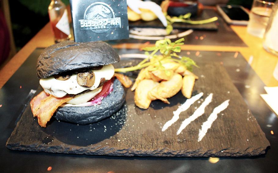 The Jurassic World-themed pop-up cafe's “Now to the Kingdom of Flames” burger features a beef patty, bacon, american cheese and mushrooms served atop black buns.