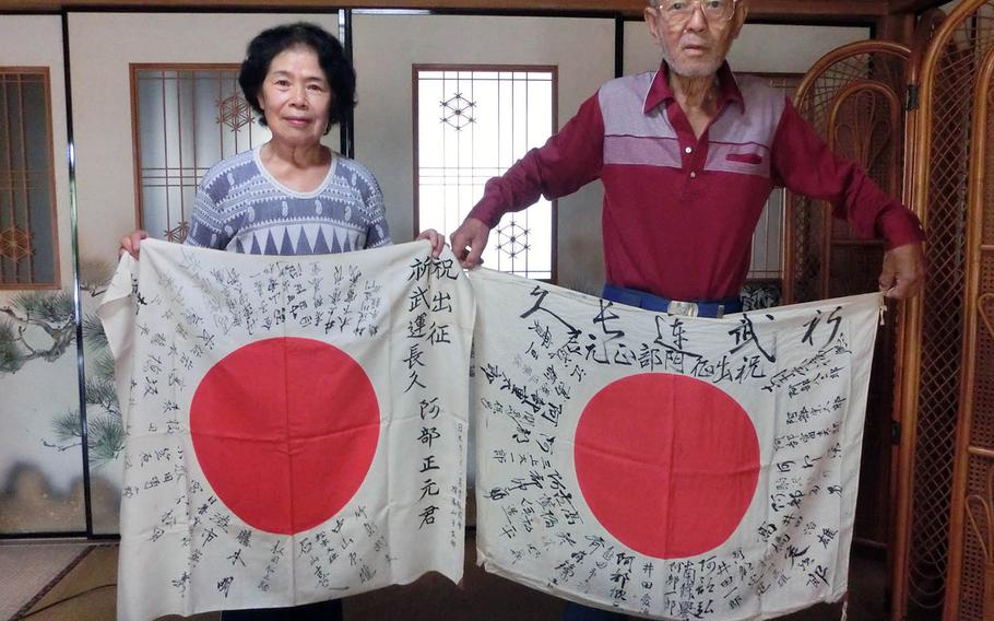 Hisashi Abe and his wife, Saeko, hold two Japanese flags that belonged to their uncle, Masamoto Abe, at their home in Yokohama, Japan, Saturday, Aug. 25, 2018.