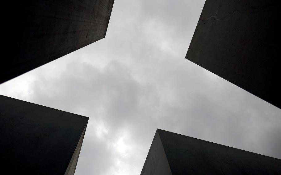 Looking up to a gray Berlin sky framed by four stelae of the Memorial to the Murdered Jews of Europe.