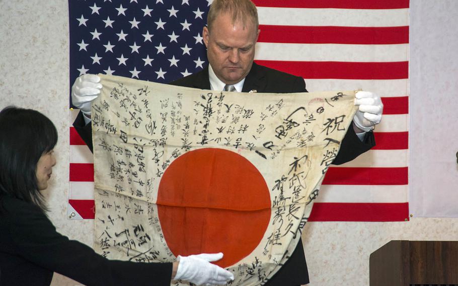 Senior Master Sgt. Lowell Armstrong unfolds a World War II-era Japanese flag during a return ceremony in Takasaki, Japan, Thursday, Feb. 14, 2019.
