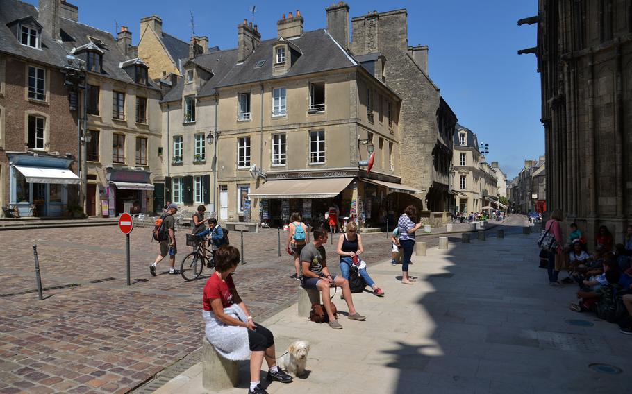 Visitors sit on a shop-lined Bayeux square, in front of the cathedral.